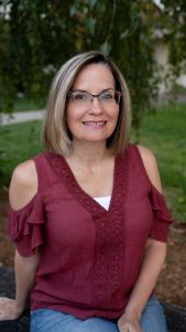 Woman with glasses smiling in a maroon top.