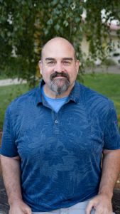 Bearded man in blue shirt outdoors.