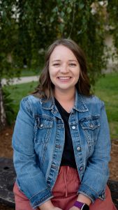 Woman in denim jacket sitting outdoors, smiling.